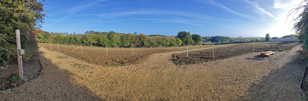 Wide lens view of the Upper Rissington Village Allotment plots prior to use. Shows trees in the far background, mud paths and wood markers.